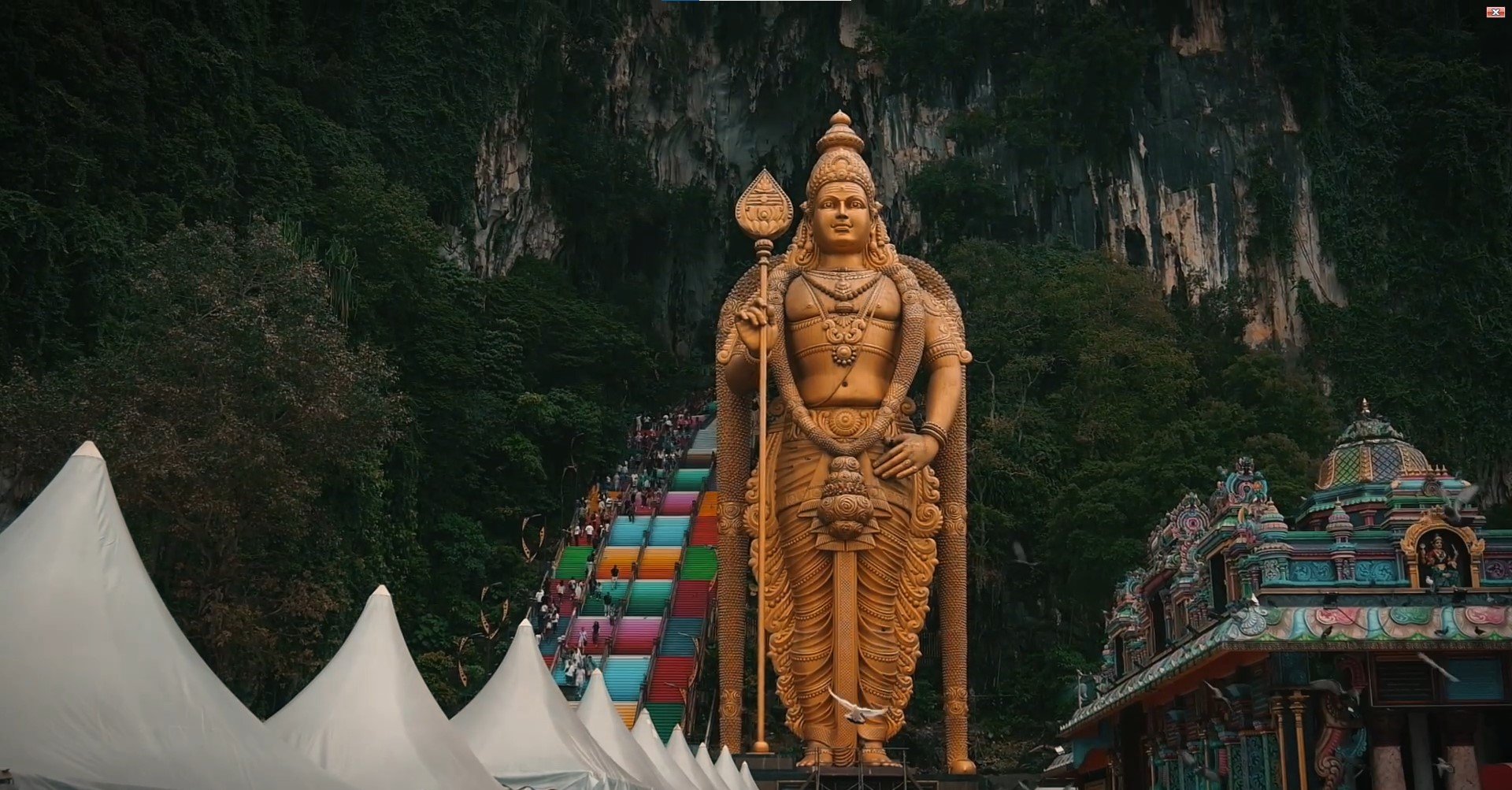 Patung emas Dewa Murugan di kaki Batu Caves di samping tangga berwarna-warni dan gopuram kuil