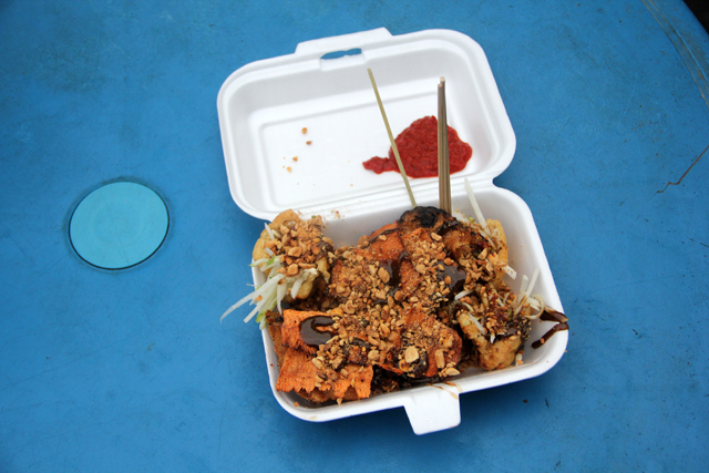 Pemanggang sate berasap dan meja yang sesak di sepanjang jalan makanan Jalan Alor pada waktu malam di Kuala Lumpur