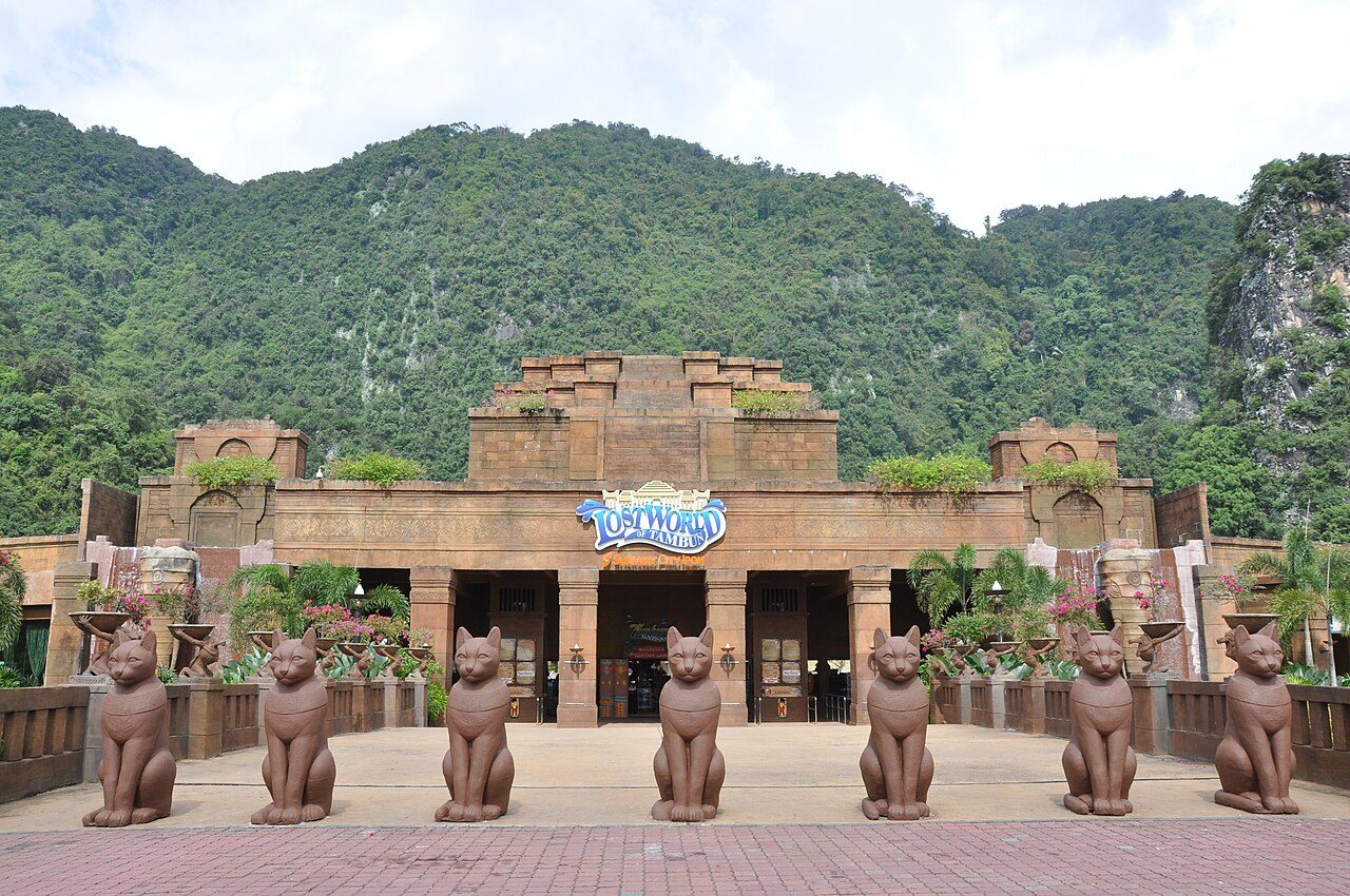Main entrance of Lost World of Tambun with rows of statues in front and forested hills behind
