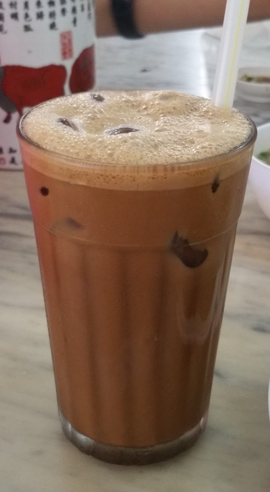 A tall glass of iced Ipoh white coffee with a foam top, one of the Ipoh drinks covered in this guide
