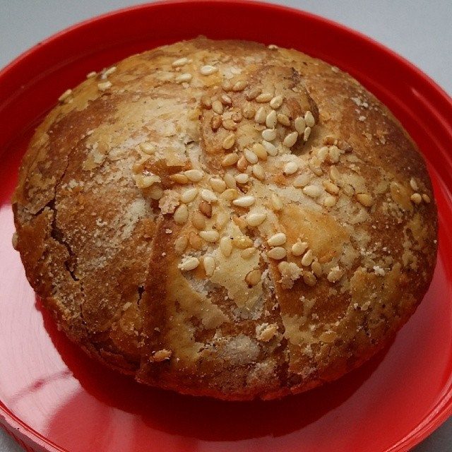 A round heong peah biscuit topped with sesame seeds on a red plate