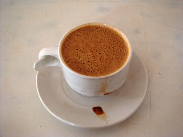 A cup of Ipoh white coffee with a creamy foam on a white saucer, one of the best-known Ipoh local products