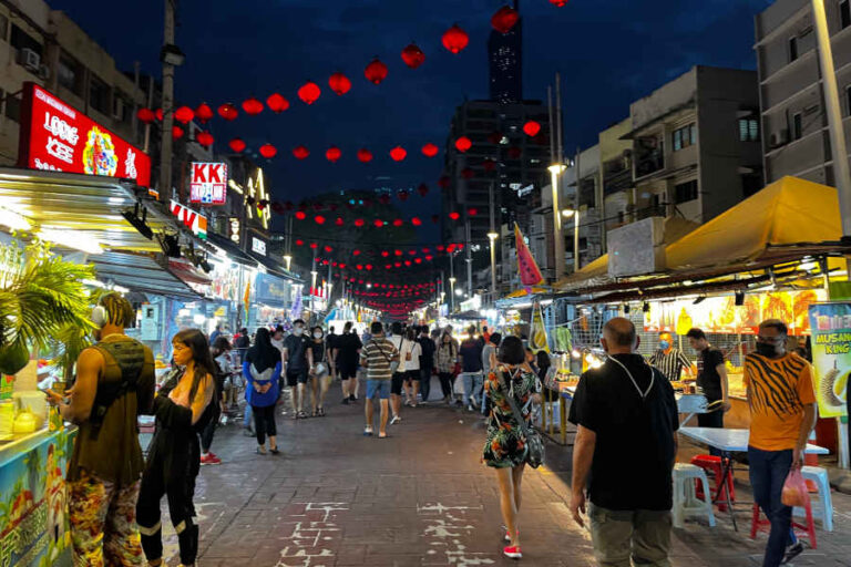 Deretan meja penjaja terbuka dan papan tanda neon di sepanjang jalan makanan Jalan Alor pada waktu malam