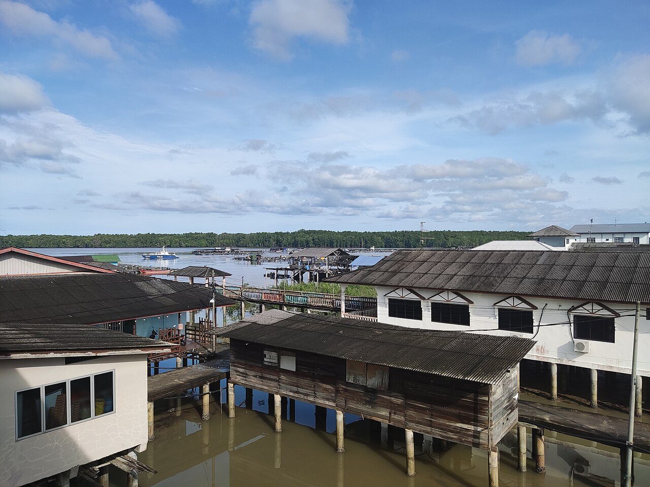 Wooden and concrete houses on stilts over the water at Kukup Laut fishing village, with mangrove forest across the channel