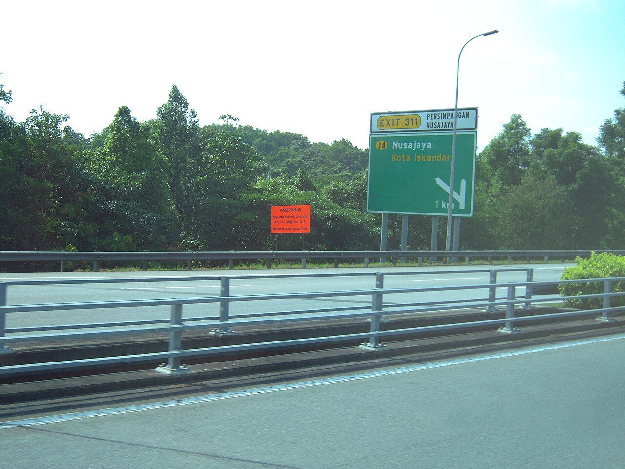 An expressway in Johor with a green exit sign for Nusajaya and Kota Iskandar beside a steel crash barrier