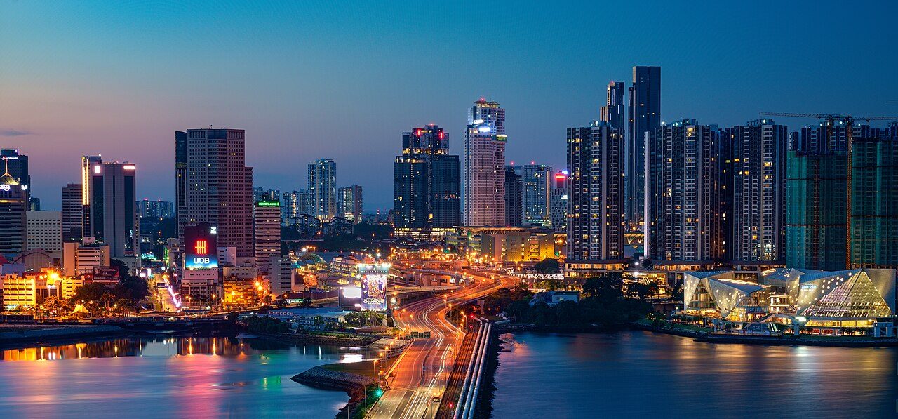 Johor Bahru nightclubs guide: the Johor Bahru city skyline at dusk with lit towers, the empty Causeway road and the glass roof of the customs complex by the water
