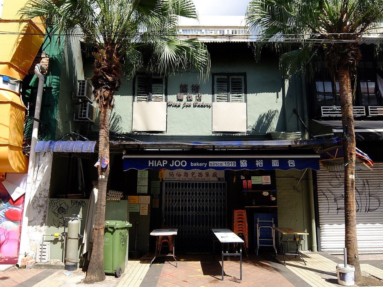 Green shophouse of Hiap Joo Bakery on Jalan Tan Hiok Nee with its blue 'since 1919' awning, photographed with the shutter closed in 2020