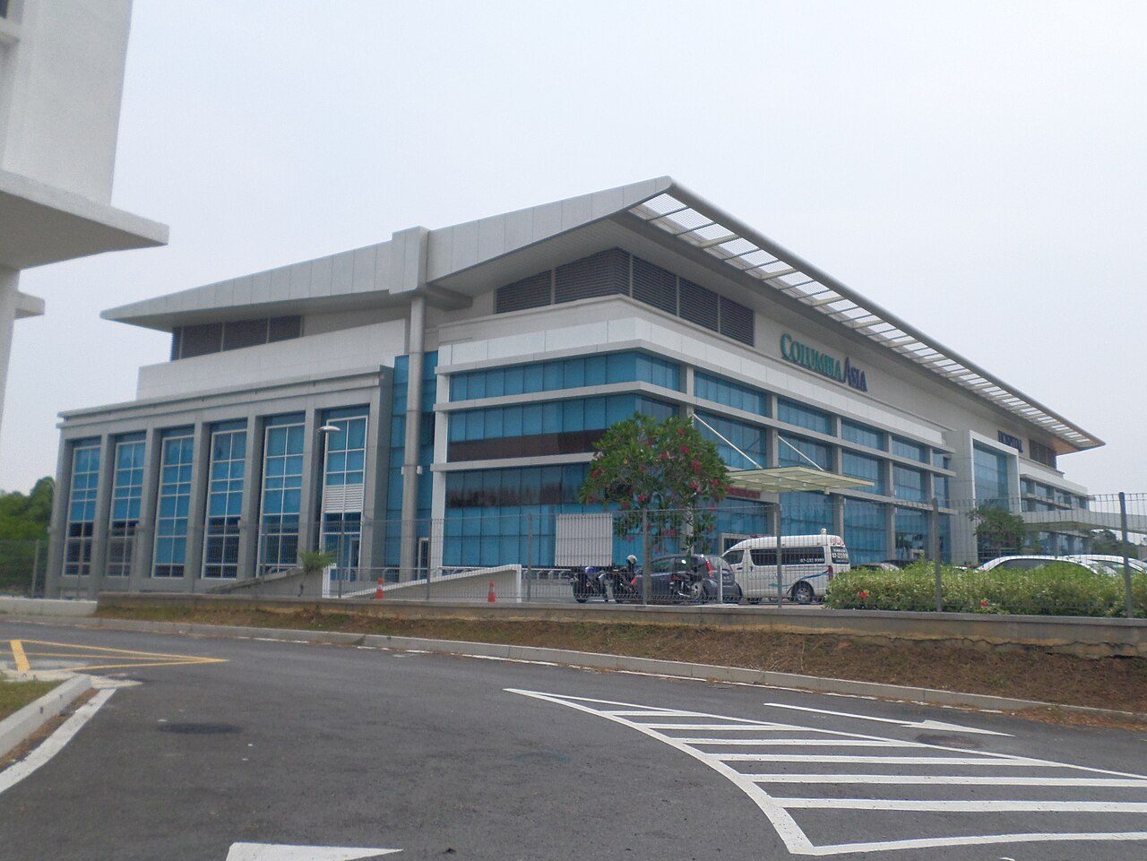 Columbia Asia Hospital Iskandar Puteri, a low white and blue-glass building with a sloping roof and the Columbia Asia name on the side