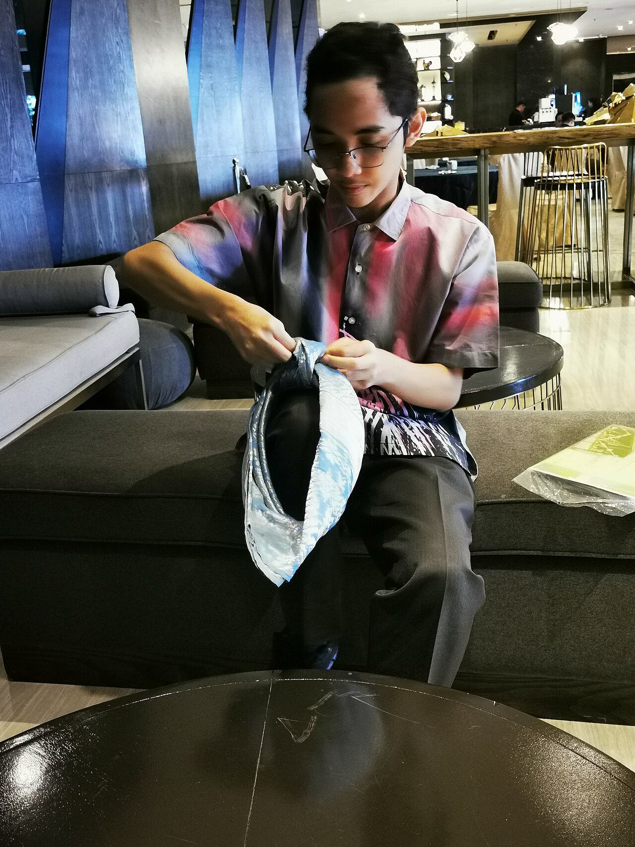 A man folding a stiff patterned cloth into a Malay tanjak headdress
