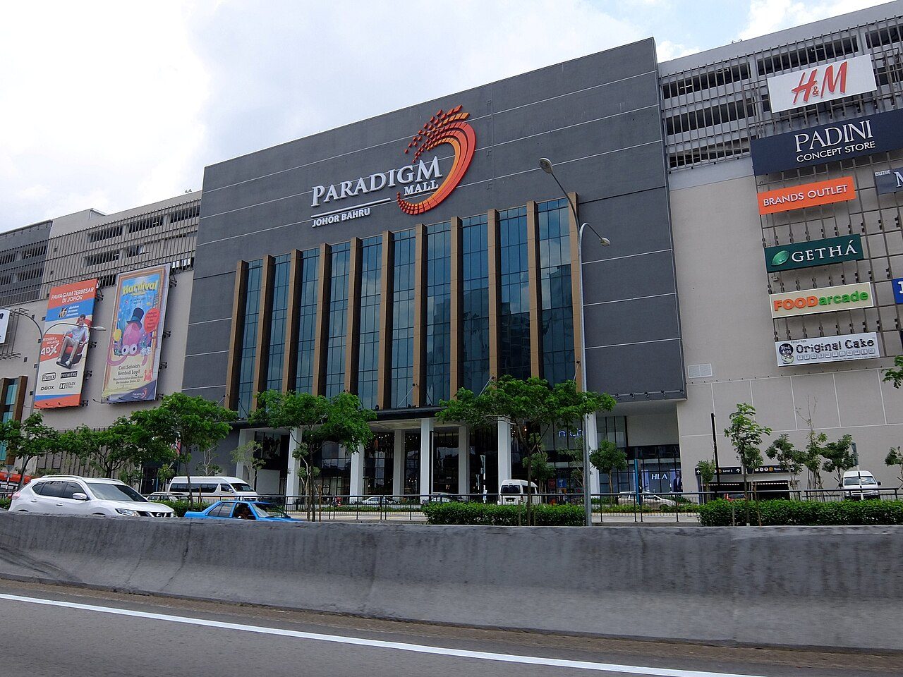 The grey front of Paradigm Mall Johor Bahru with its red swirl logo, brand signs for H&amp;M and Padini, and the main road in front
