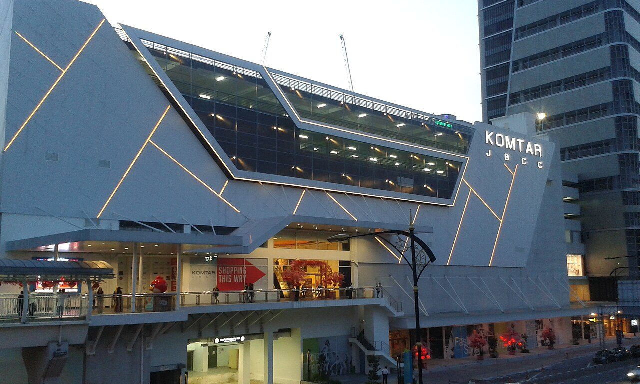 Komtar JBCC at dusk, with its angular glass and metal front and the KOMTAR JBCC sign, beside the older Komtar tower