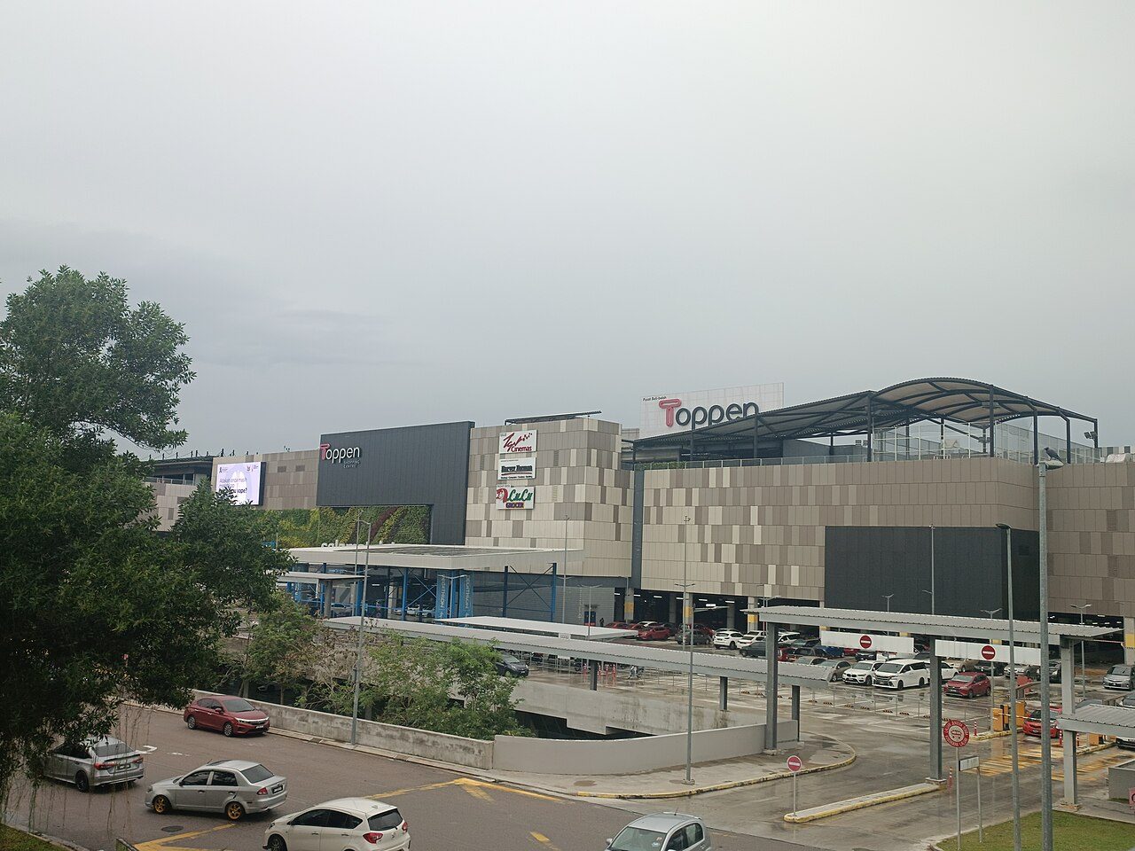 Toppen Shopping Centre in Tebrau seen across a car park and covered bus stop on a grey day, with the Toppen sign on the building