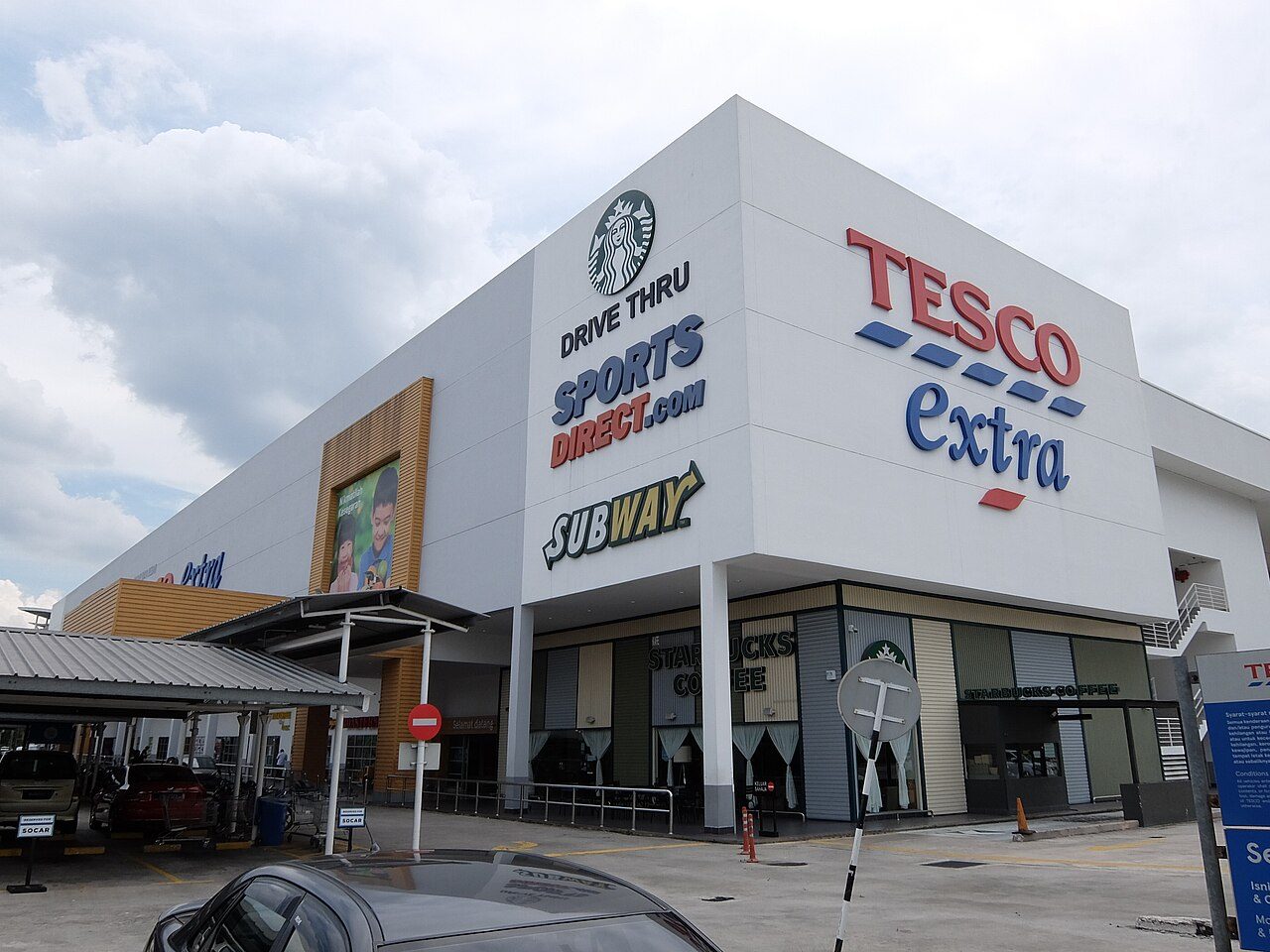 The hypermarket at Desa Tebrau in 2019, when it was still branded Tesco Extra, with Starbucks drive-thru, Sports Direct and Subway signs