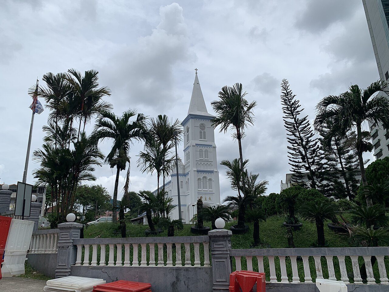 The white bell tower of the Church of the Immaculate Conception in Johor Bahru rising above palm trees on a grassy slope