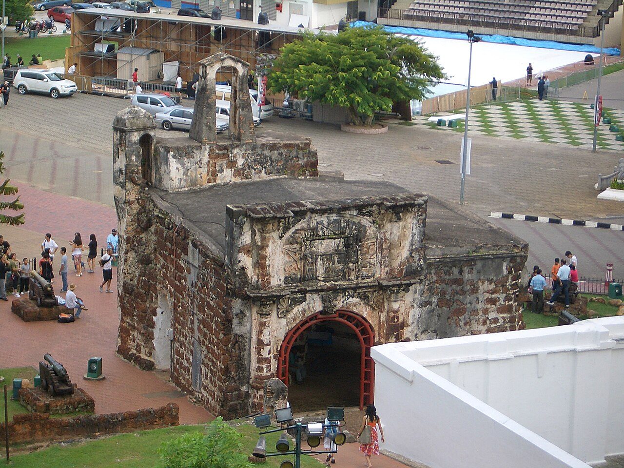 The stone Porta de Santiago gateway of A Famosa with visitors on the lawn behind it