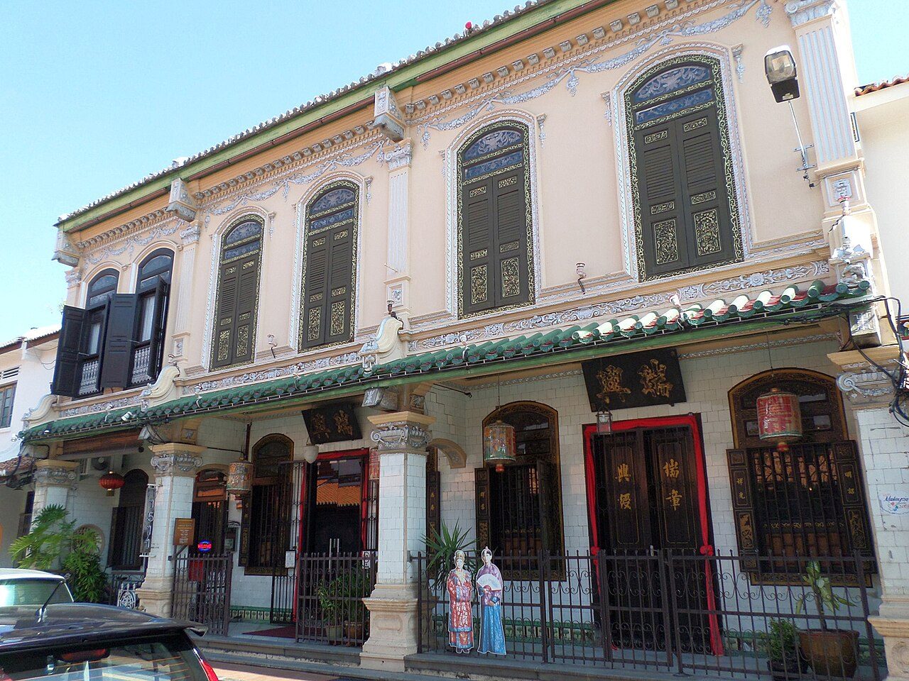 The ornate cream facade of the Baba and Nyonya Heritage Museum with carved doors and green shutters