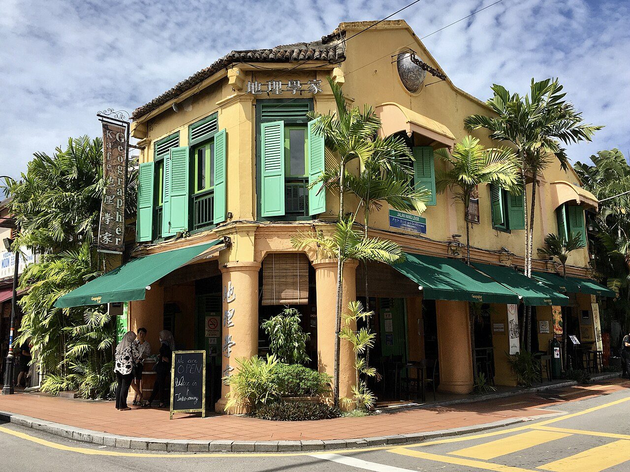 The Geographér Café corner shophouse on Jonker Street in Melaka, with green shutters, green awnings and palm trees