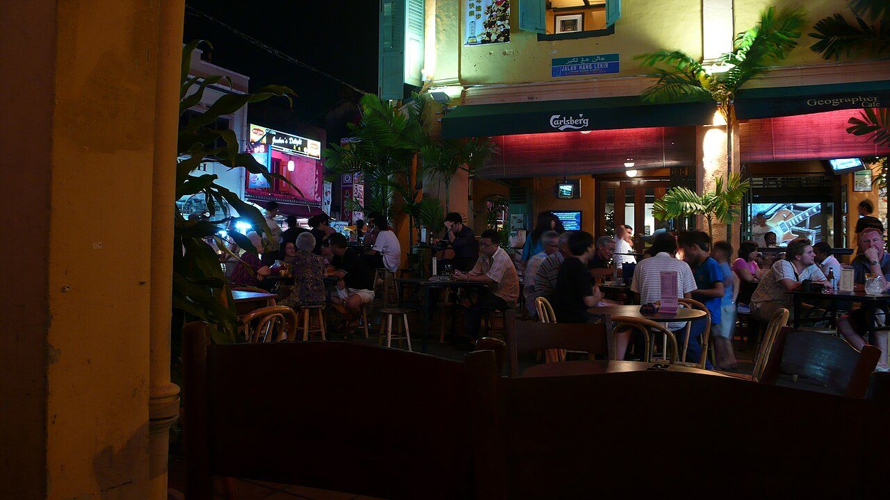 Melaka bars: people drinking at the outdoor tables of a corner bar lit up at night in Melaka's Chinatown