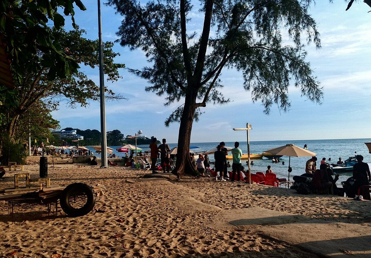 Beach umbrellas, trees and swimmers along the sand at Teluk Kemang Beach, Port Dickson