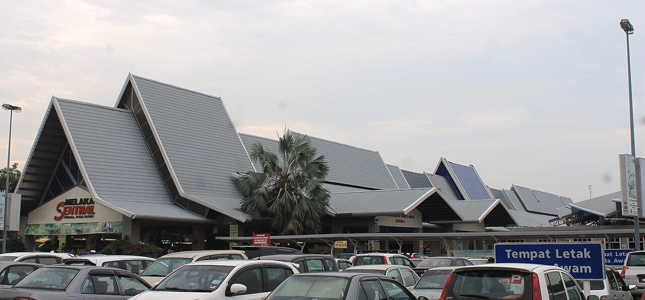 Car rental in Melaka: the main building of Melaka Sentral bus terminal with its tiered grey roofs and a full car park in front