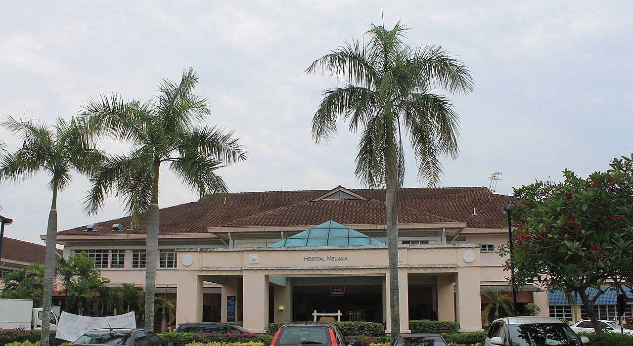 Melaka hospitals: the main entrance of Hospital Melaka, a low building with a tiled roof and a glass canopy, behind tall palm trees