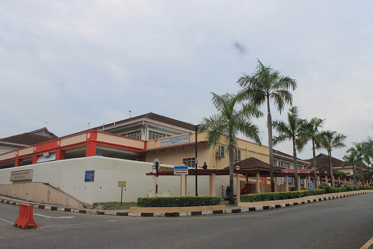 The Emergency and Trauma Department building of Hospital Melaka, with its red and cream entrance and a row of palm trees
