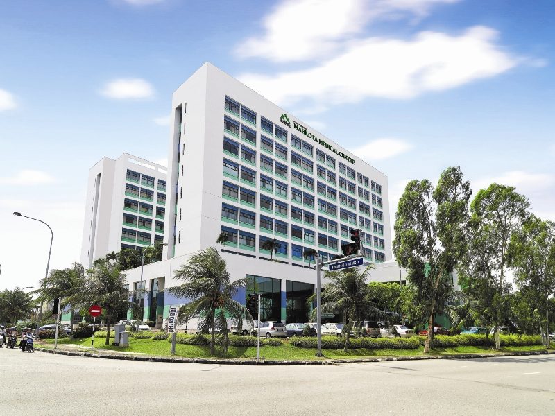 The white Mahkota Medical Centre tower in Melaka with its name on the facade, seen from a road junction