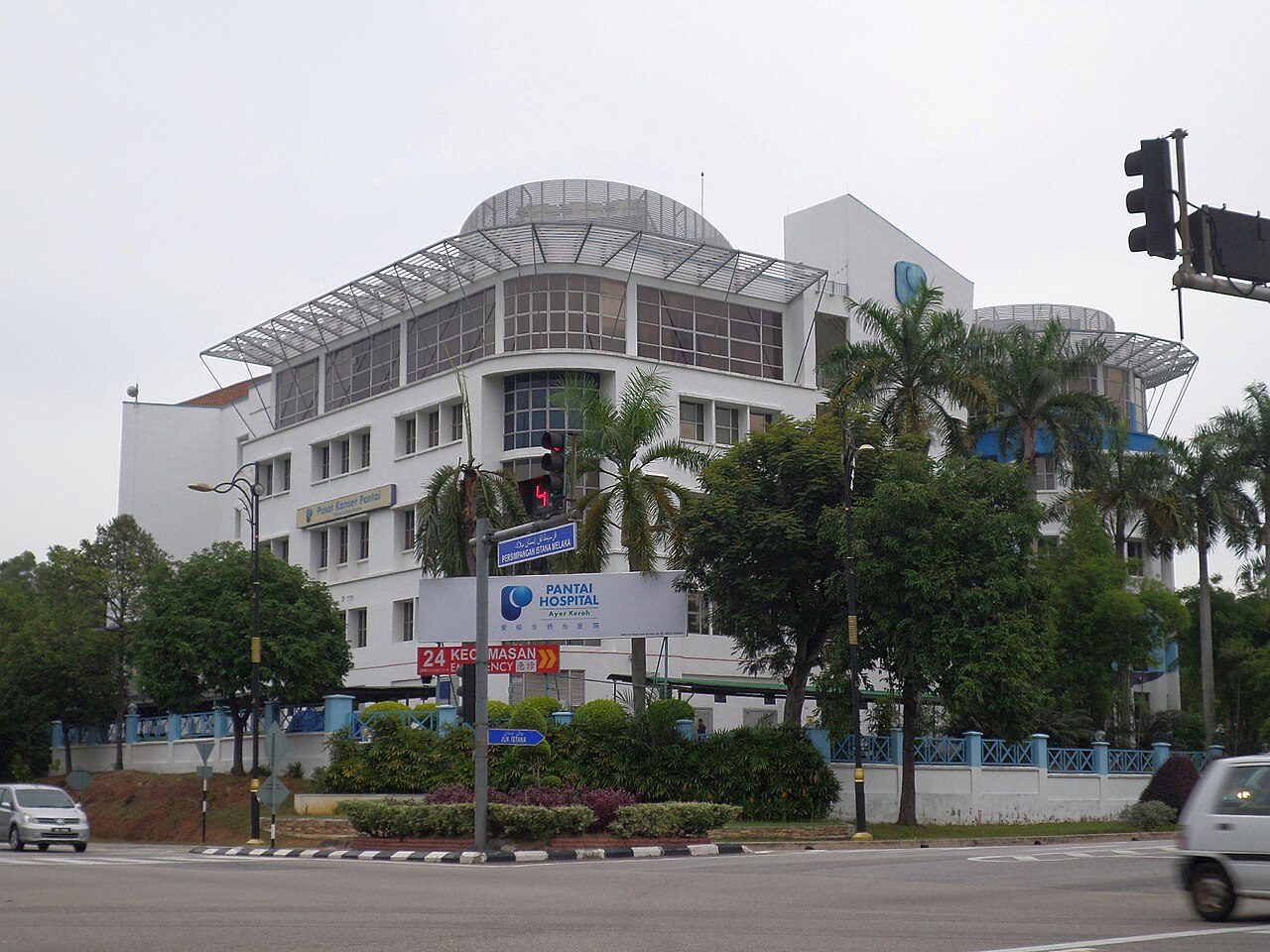 Pantai Hospital Ayer Keroh, a white building with a curved roof canopy, and a 24-hour emergency (Kecemasan) sign at the junction