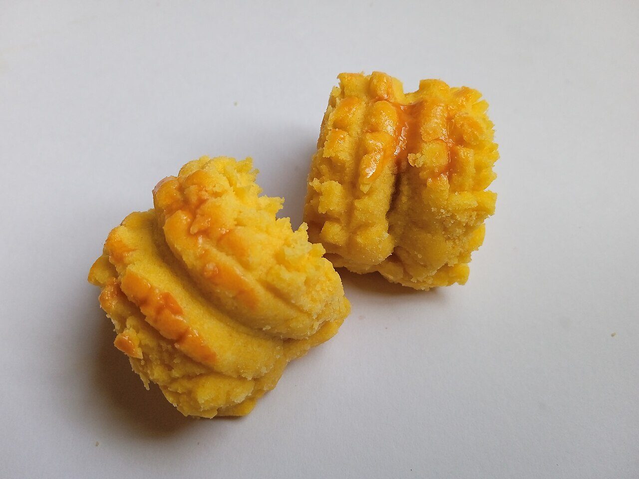 Two golden Malaysian-style pineapple tarts with ridged pastry rolled around pineapple jam