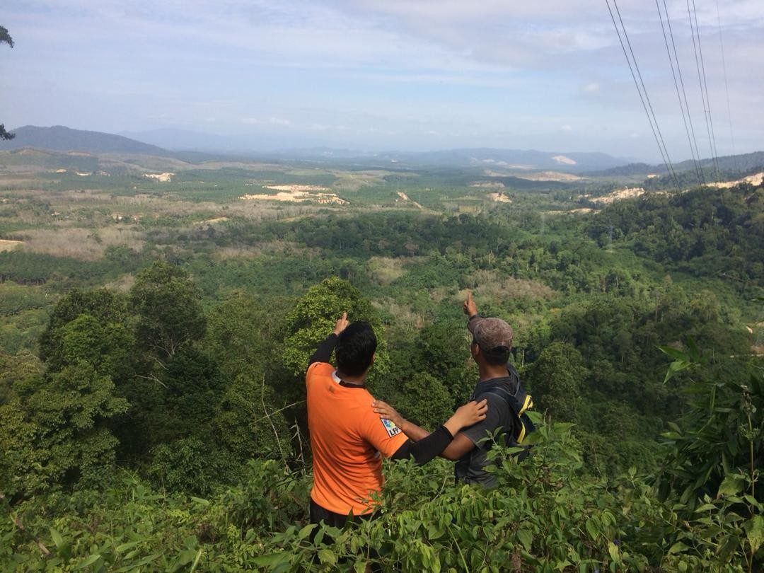Two hikers pointing out over forested hills and plantations from a viewpoint at Bukit Batu Lebah