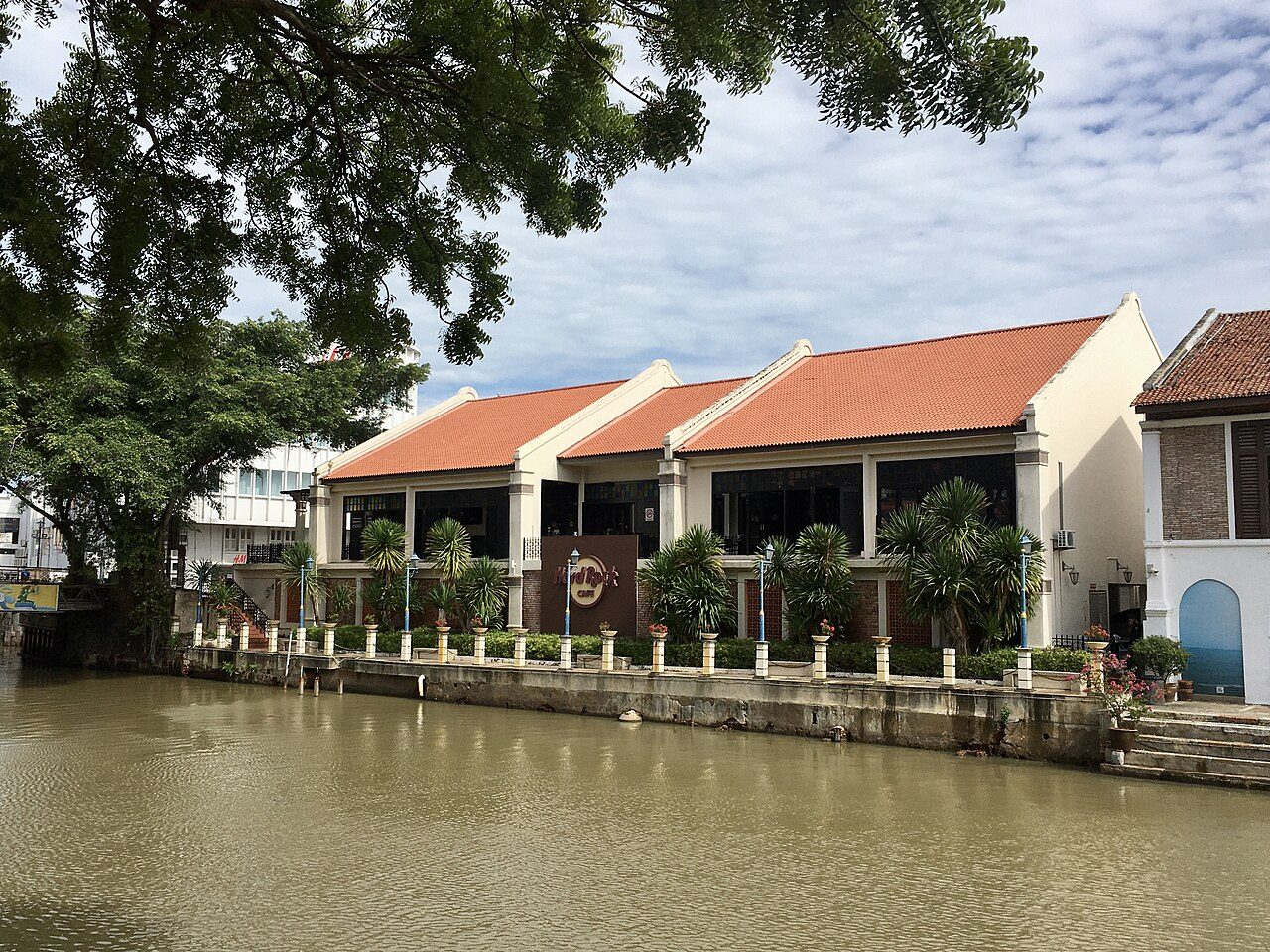Hard Rock Cafe Melaka, a row of cream buildings with orange tiled roofs and a Hard Rock sign on the bank of the Melaka River