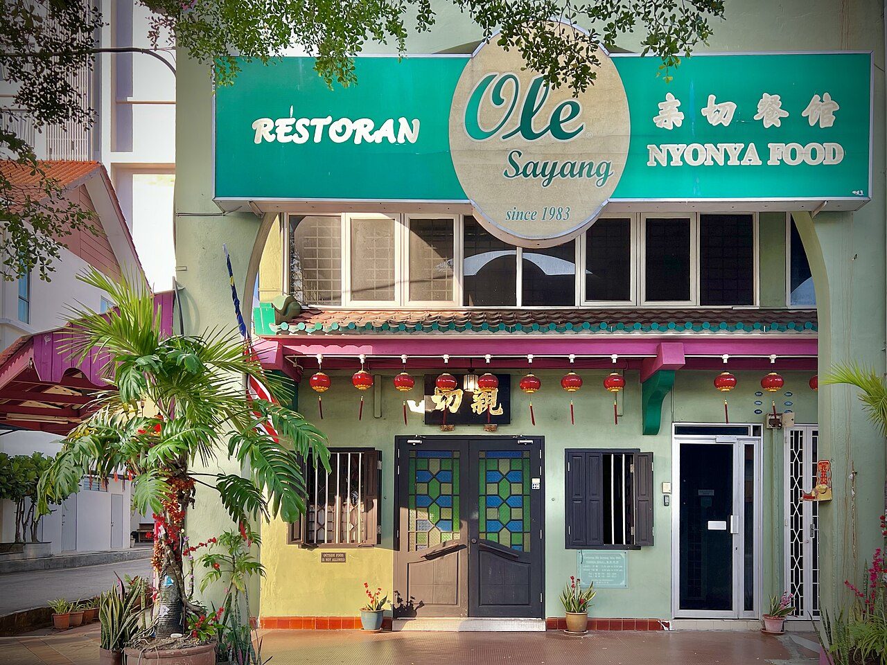 The green shophouse front of Restoran Ole Sayang Nyonya Food in Melaka, with its round sign reading since 1983 and red lanterns over the door