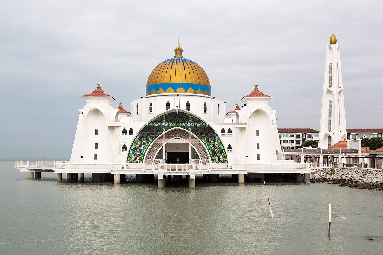 The white Melaka Straits Mosque with a golden dome and stained-glass arch standing on stilts over the sea