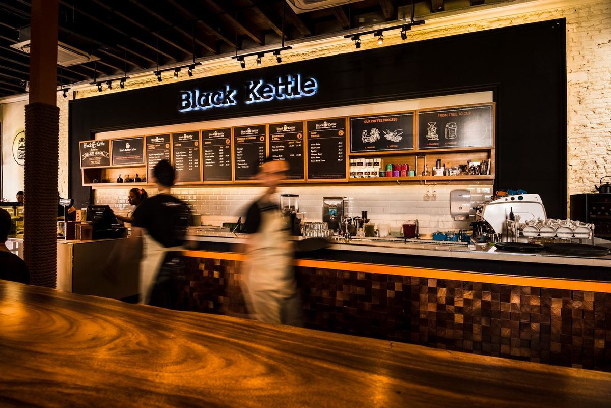 槟城乔治市 Beach Street 的 Black Kettle 咖啡馆内，Black Kettle 招牌下的咖啡与点餐柜台