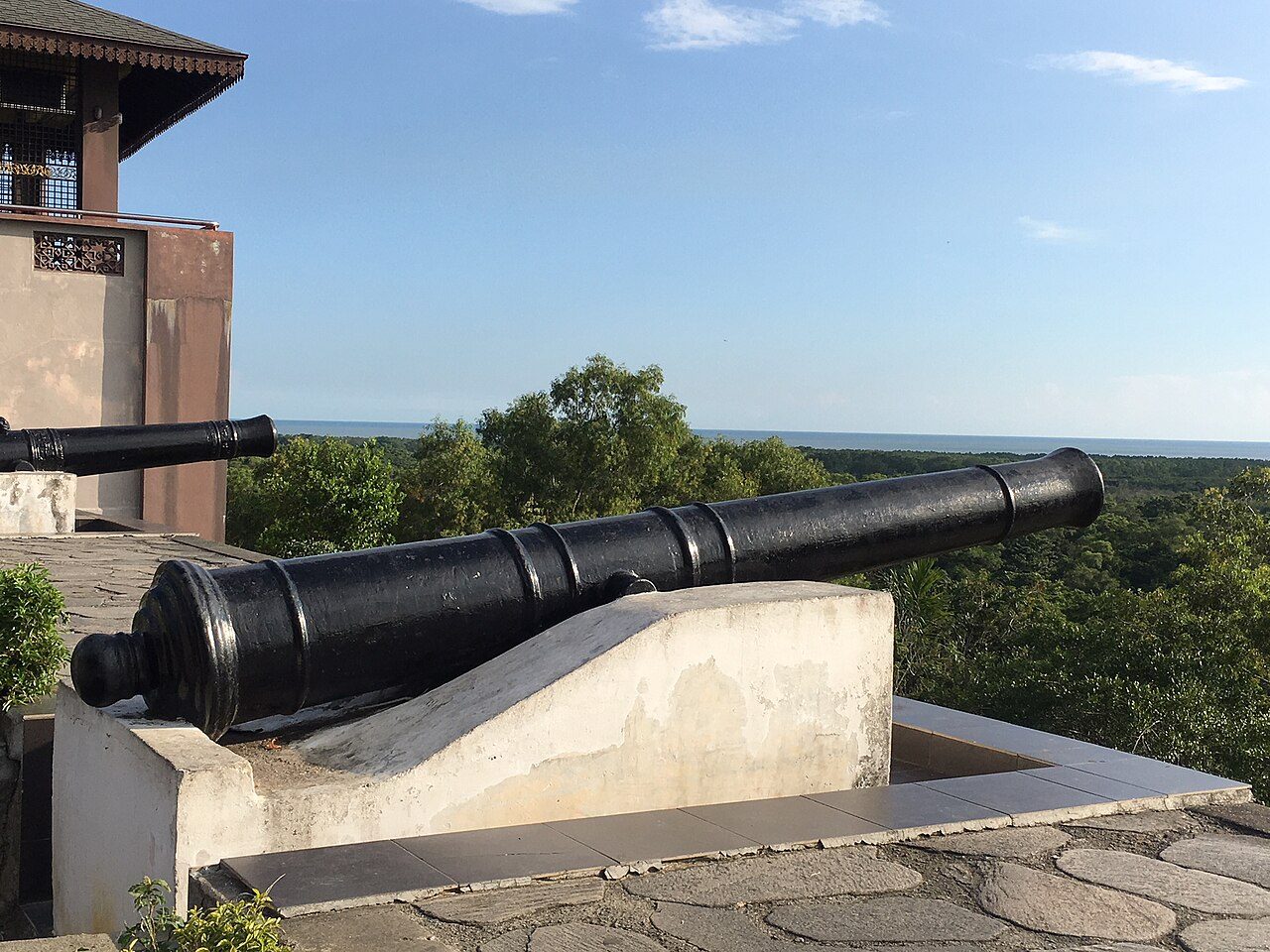 Old black cannon on the hilltop at Bukit Melawati pointing over the trees towards the Strait of Malacca, Kuala Selangor