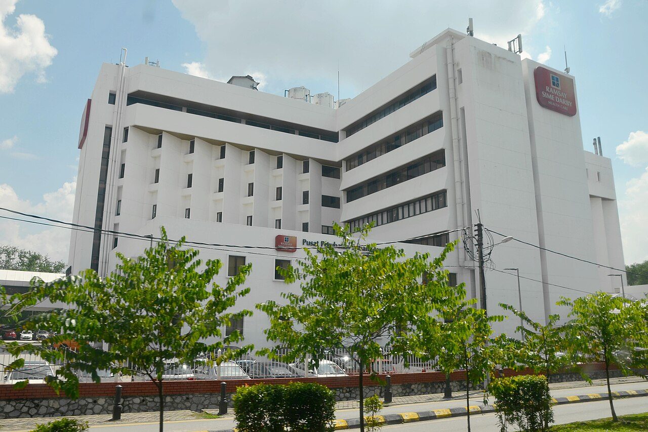 The white Subang Jaya Medical Centre building with older Ramsay Sime Darby Health Care signs, seen from the road