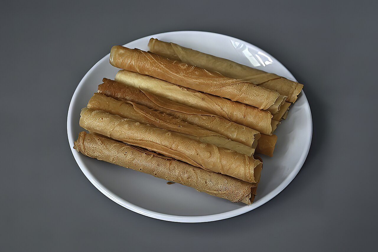 Rolled kuih kapit egg-roll biscuits stacked on a white plate