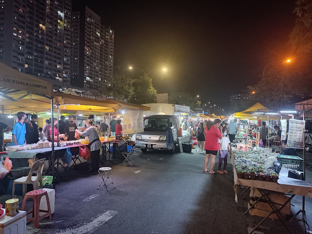 Stalls under yellow canopies and shoppers on a closed street at night at a pasar malam in Seri Kembangan, one of the night markets in Selangor