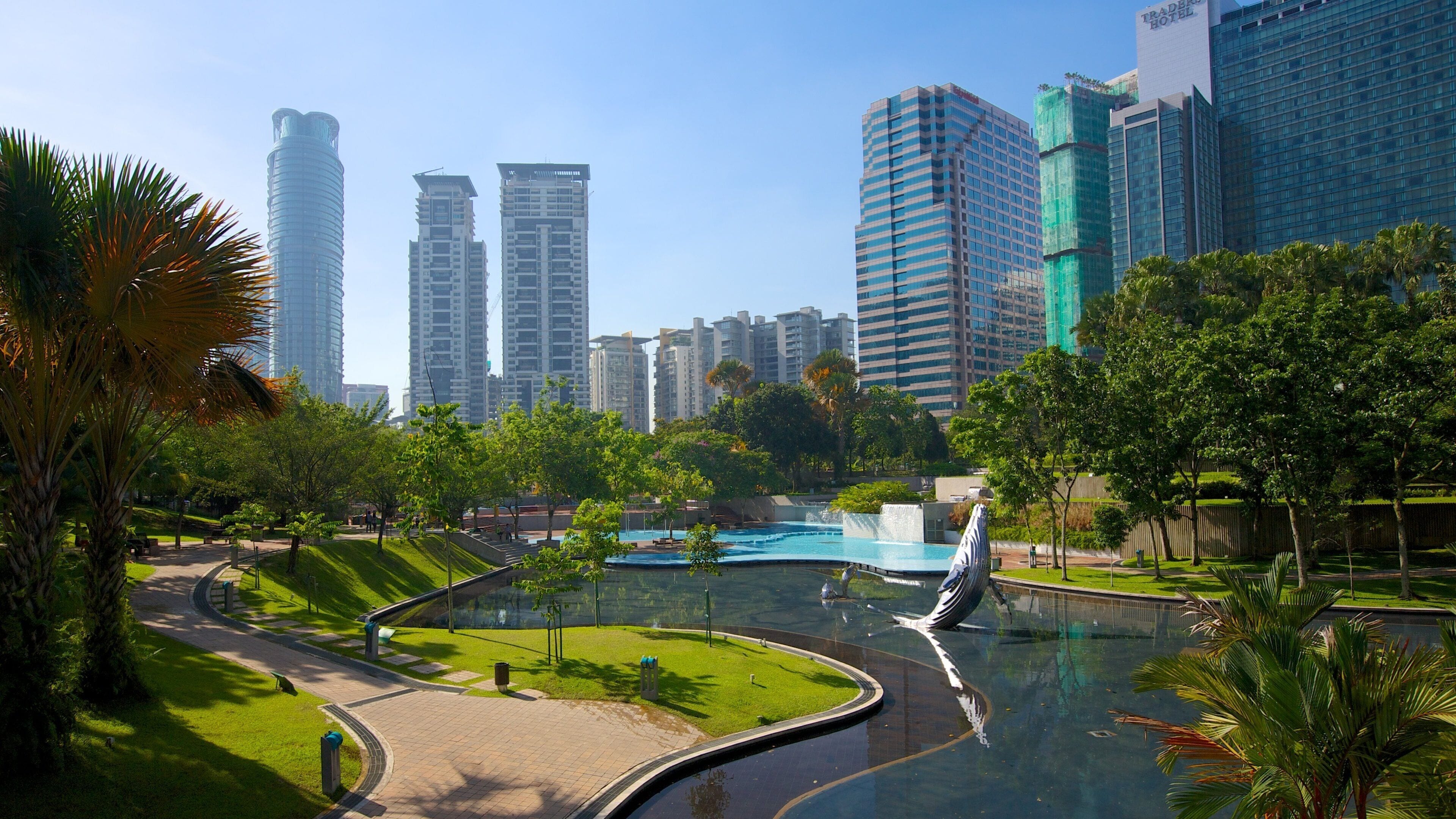Halaman rumput, laluan pejalan kaki dan kolam pantulan Taman KLCC dengan menara pejabat Kuala Lumpur di belakang
