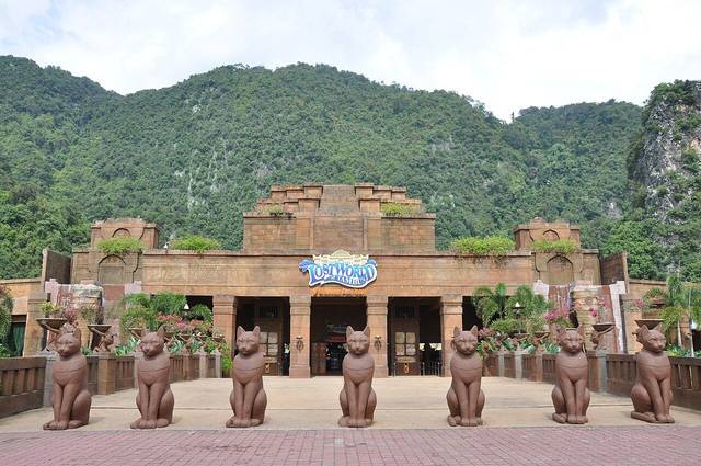 Main entrance of Lost World of Tambun with rows of statues in front and forested hills behind