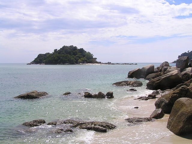 Rocks on the shore at Teluk Nipah with small, wooded Giam Island offshore