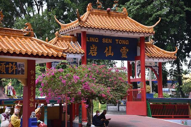 Red-pillared gate of Ling Sen Tong temple with blue sign, orange roof tiles and pink bougainvillea