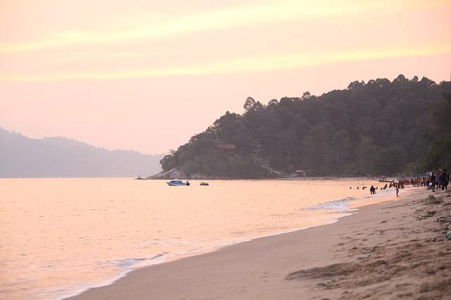 Pink evening light on the beach at Teluk Batik with a forested headland and swimmers at the water's edge