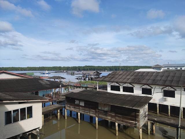 Wooden and concrete houses on stilts over the water at Kukup Laut fishing village, with mangrove forest across the channel