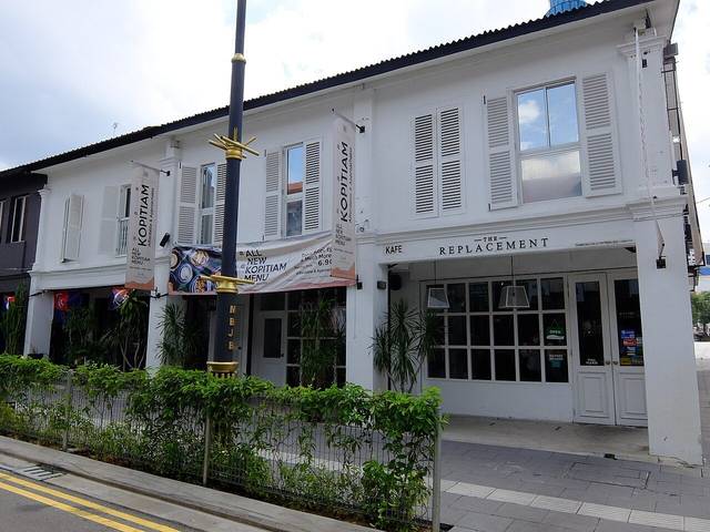 White two-storey shophouse of The Replacement on Jalan Dhoby, Johor Bahru, with shuttered windows and a cafe sign above the glass doors, photographed in 2021