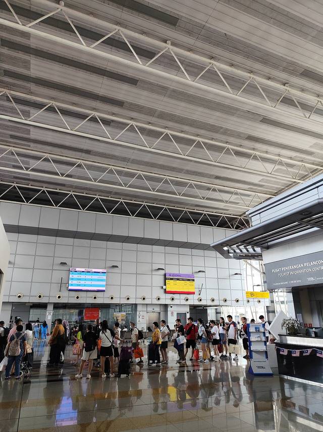 The concourse of JB Sentral station under a high white roof, with travellers queuing at the departure gates for the cross-border Shuttle Tebrau train