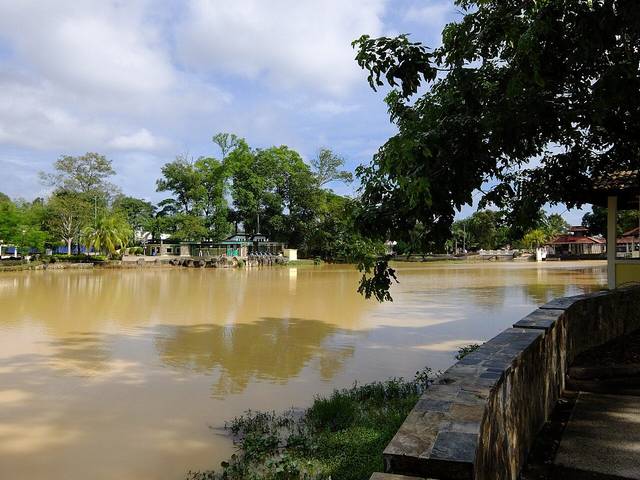 The brown lake at Taman Merdeka in Johor Bahru, with trees and park pavilions on the far bank