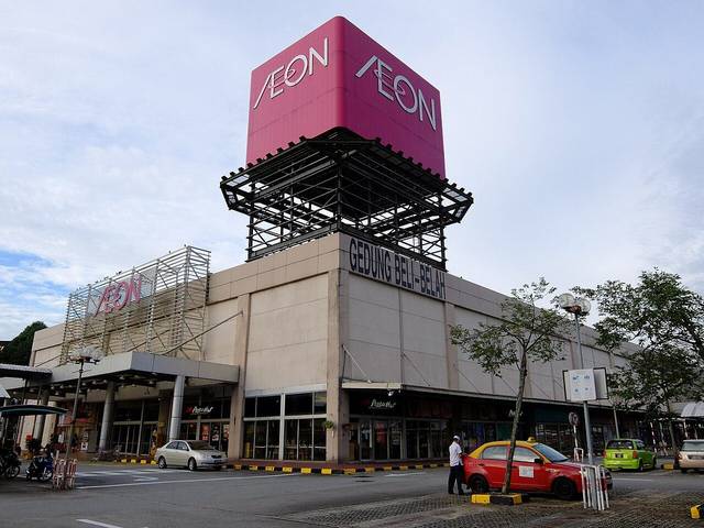 AEON Permas Jaya with its pink AEON sign tower above the grey mall building and a taxi parked in front