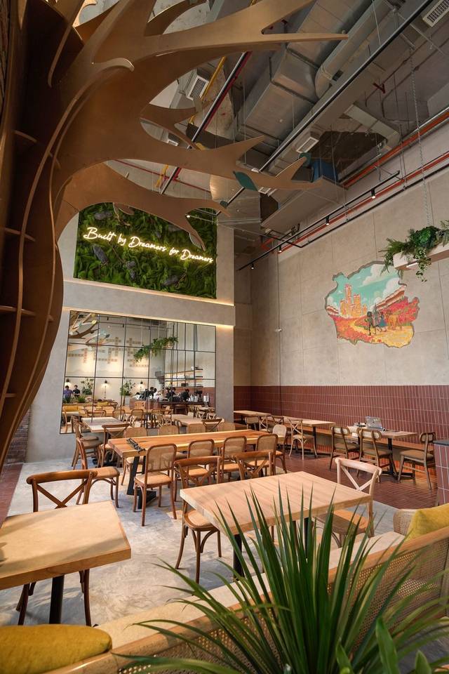 Dining room of Yellow Brick Road Chinatown, Kuala Lumpur, with a wooden tree sculpture, moss wall and KL skyline mural