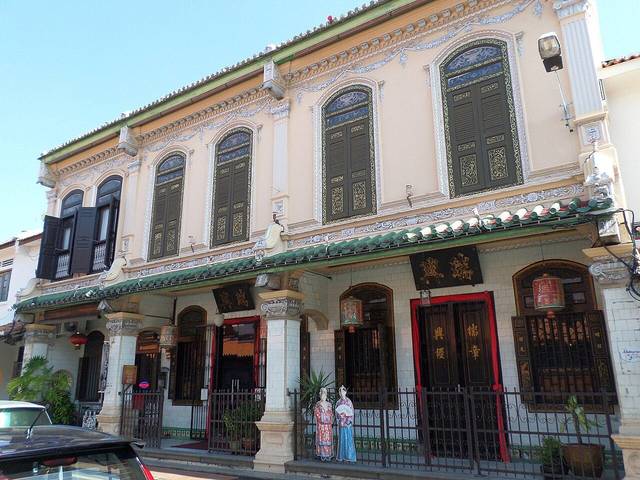 The ornate cream facade of the Baba and Nyonya Heritage Museum with carved doors and green shutters